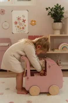 Kind spielt liebevoll mit dem rosa Holzpuppenwagen von Little Dutch im Kinderzimmer.